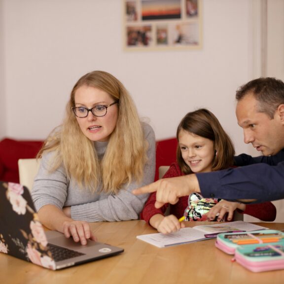 Image of a woman and a man sat round a computer pointing with a young child.