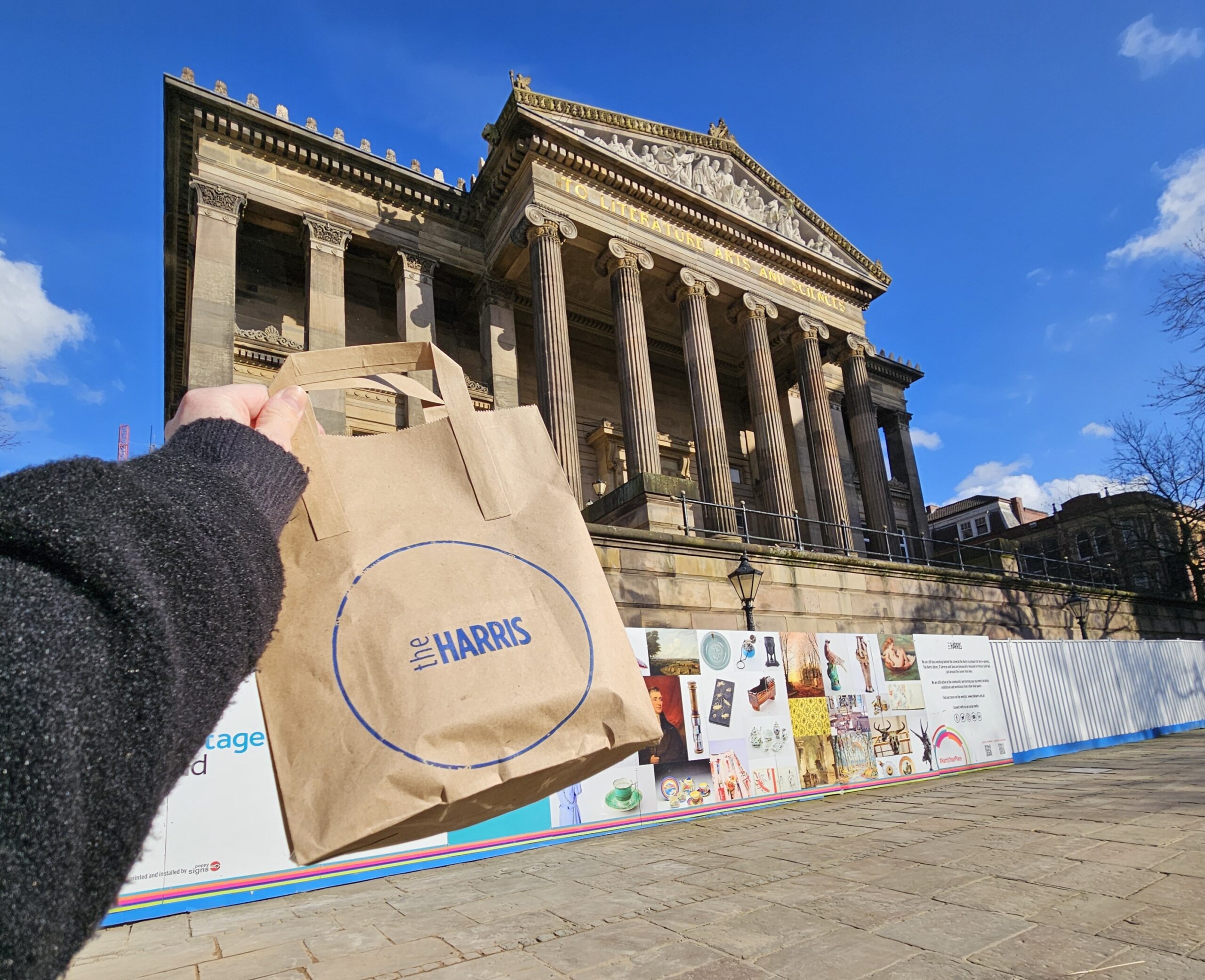A small brown gift bag being held up in front of the Harris building.