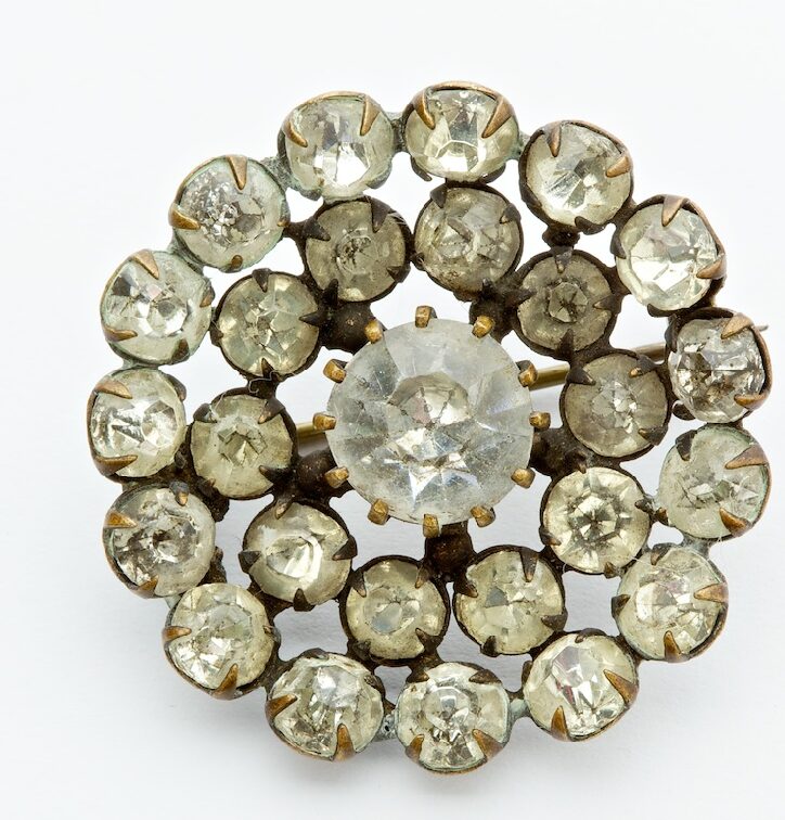 A circular brooch, featuring a circular pattern of intimation diamonds and one larger diamond.