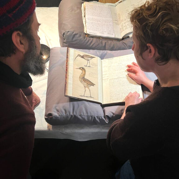 Two people lean over a book displaying illustrations of birds.