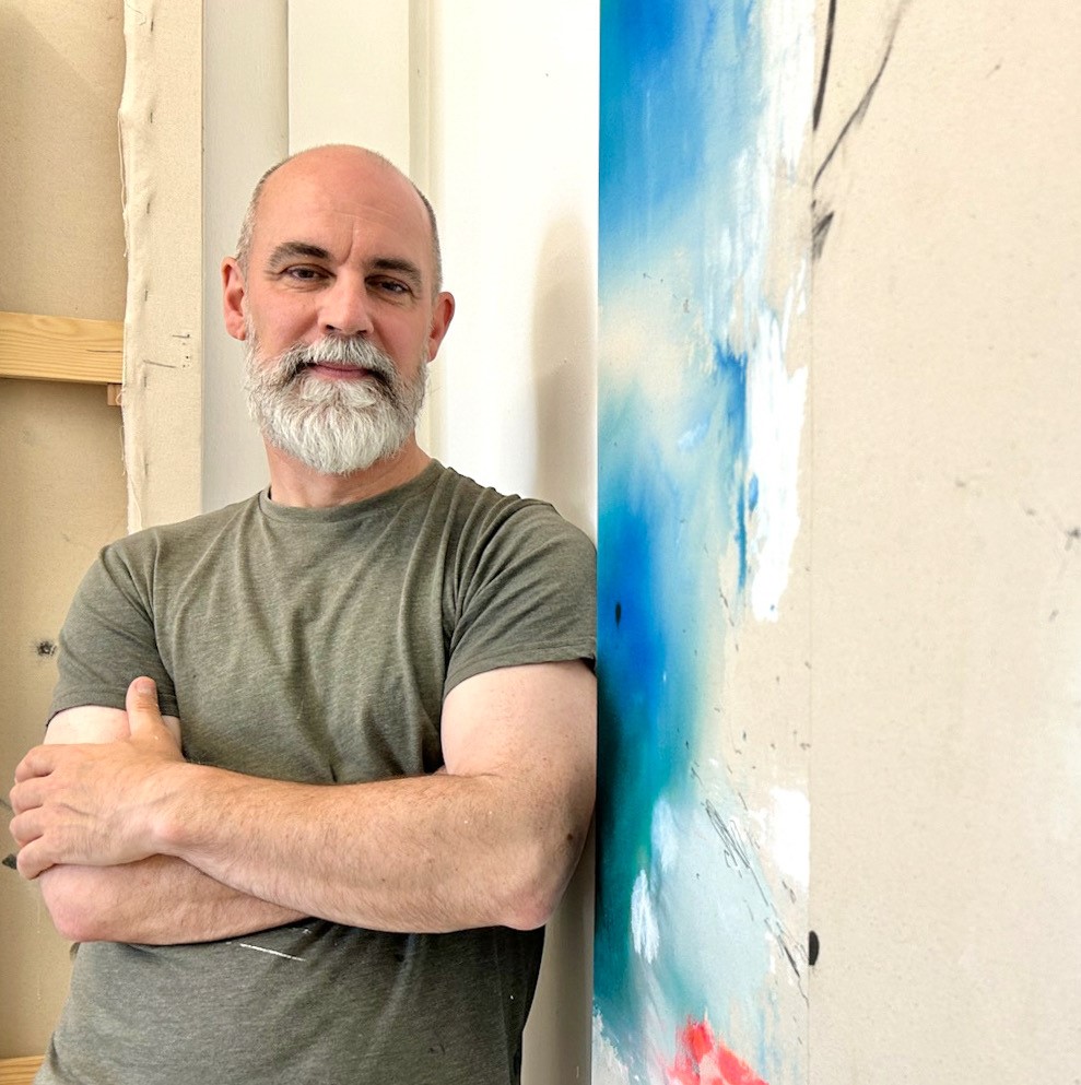 A person wearing a khaki t-shirt leans against a piece of blue artwork.
