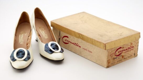 A pair of cream shoes with a black bow.