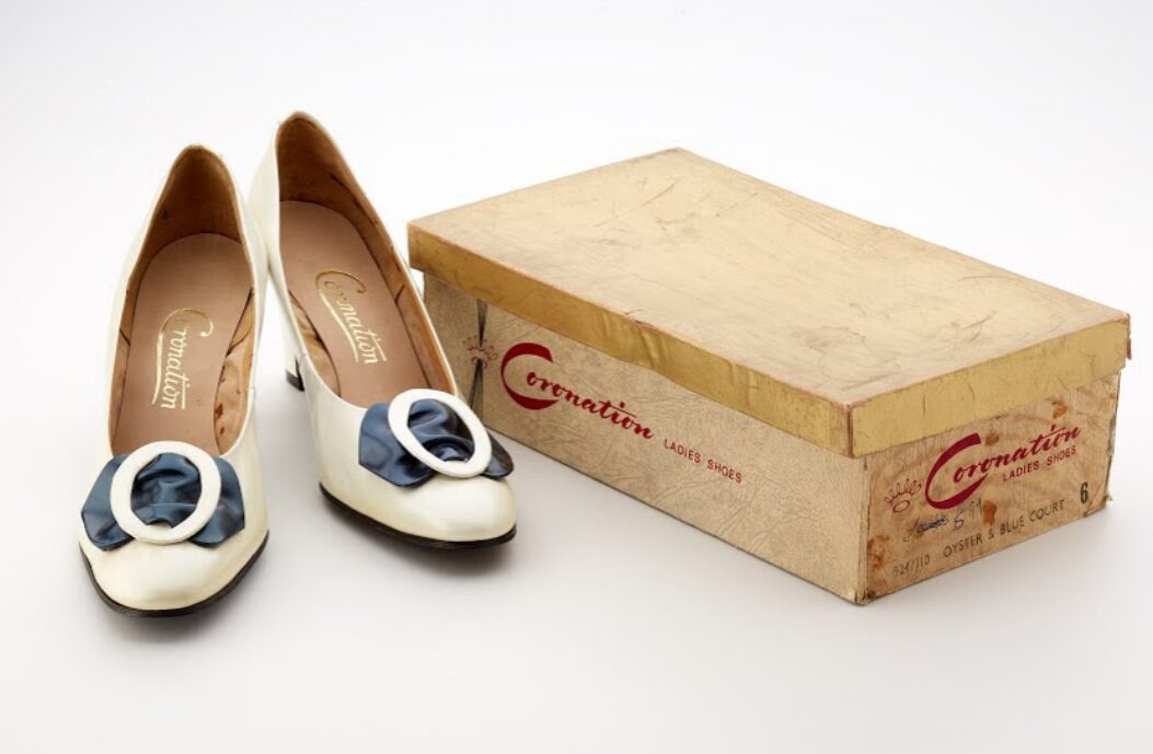 A pair of cream shoes with a black bow.