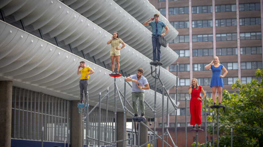 A group of performers stood on scaffolding in front of the bus station.